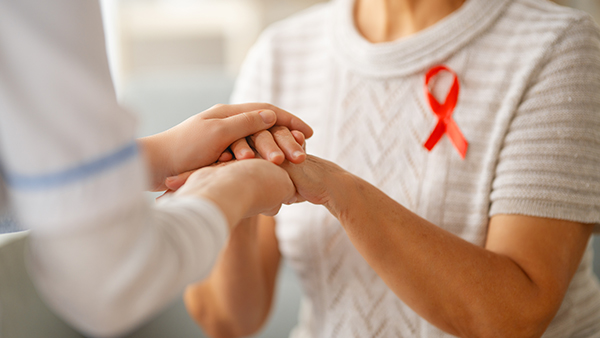 A person holds another's hands; one is wearing a white knit sweater with a red ribbon.